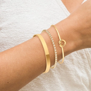 Set of three golden bangles including polished wide cuff and shimmering tennis bracelet