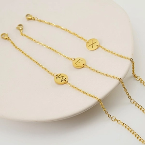 Detalle de tres pulseras minimalistas con iniciales bañadas en oro sobre bandeja blanca
