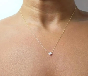 Close-up of minimalist gold chain necklace with a round white diamond pendant on neck