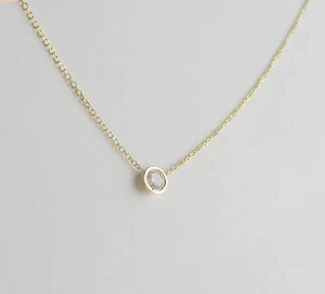 Detailed close-up of a minimalist gold necklace featuring a round bezel-set zircon pendant