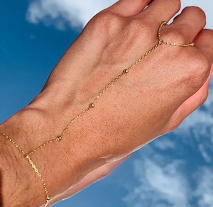 Close-up of elegant gold bead finger bracelet jewelry worn against a sunny sky background