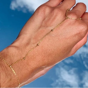 Elegant gold slave bracelet with beads and ring worn on hand against blue sky