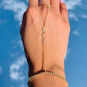 Elegant gold slave bracelet with beads and three zircon stones against a blue sky background