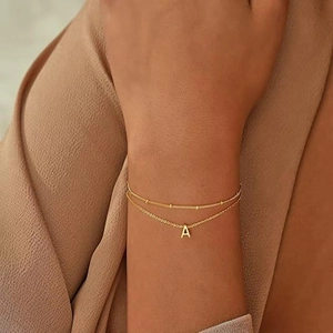 Dettaglio del bracciale a doppio strato dorato con iniziale A e perline su un polso
