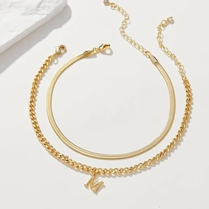 Detail of layered gold stainless steel snake chain and M letter pendant with lobster clasp
