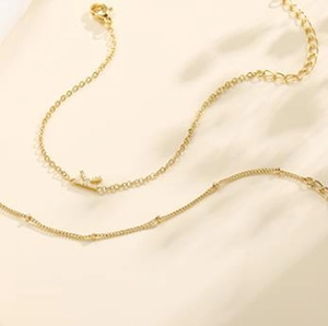 Detail of layered gold stainless steel chains with a crystal M initial pendant and bead link