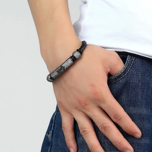 Close-up of men's black braided leather bracelet with pavé zircon metal charm on wrist