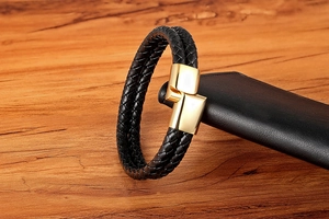 Detail of woven black leather bracelet with a polished gold magnetic metal clasp