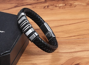 Detailed view of woven black leather bracelet with silver metal charms on a gift box
