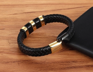 Detail of men's black braided leather bracelet with gold magnetic clasp on wooden desk