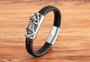 Detail of a braided black leather bracelet with silver skull charm and magnetic metal clasp