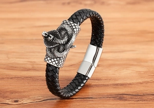 Close-up of braided leather bracelet with silver cobra charm and magnetic clasp on wood