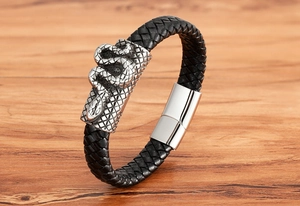 Close-up of black braided leather bracelet with silver snake charm on wood background