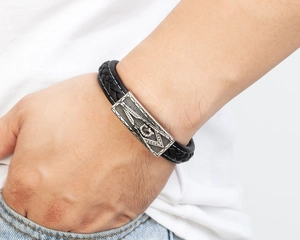 Detail eines geflochtenen Lederarmbands mit Freimaurer-Symbol auf einer silbernen Metallplatte