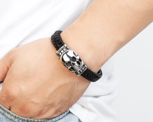 Close-up of a men's black braided leather bracelet with a silver skull head charm detail