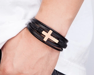 Detailopname van een gelaagde zwarte leren herenarmband met een gouden kruis om de pols