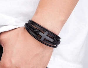 Detail van een meerlaagse zwarte lederen herenarmband met een matgrijs metalen kruis