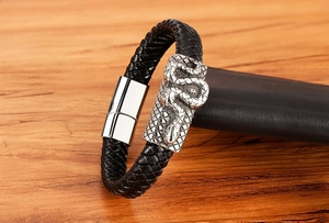 Detail of men's black braided leather bracelet featuring a silver snake relief and magnetic clasp