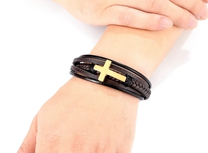 Detailopname van meerlaagse gevlochten lederen armband met gouden metalen kruisdetail