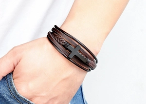 Detailopname van herenarmband met meerdere lagen donkerbruin leer en zwart kruis