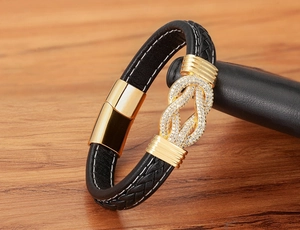 Detail eines schwarzen geflochtenen Lederarmbands mit Goldknoten und Zirkonia-Inlay