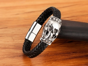Detail of black braided leather men's bracelet featuring a silver skull and magnetic clasp