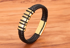 Close-up of black braided leather men's bracelet with gold magnetic clasp on wooden desk