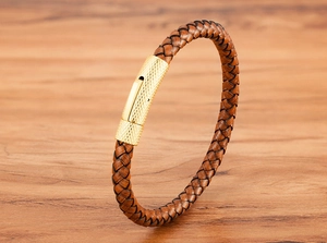 Détail du bracelet en cuir tressé marron avec fermoir en métal doré sur du bois