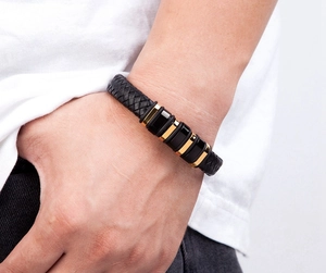 Close-up of men's braided black leather bracelet with gold and black metal clasp