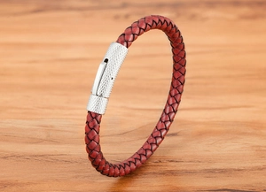 Détail d'un bracelet en cuir tressé rouge avec fermoir en métal argenté texturé sur bois