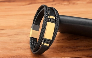 Detail eines mehrlagigen schwarzen Lederarmbands mit goldenem Magnetverschluss und Platte