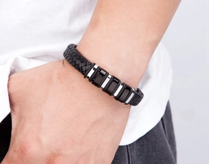 Detailed view of men's braided black leather bracelet with metallic cylinders on a wrist