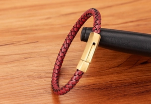 Detail view of red braided leather bracelet with golden metallic magnetic clasp on wood