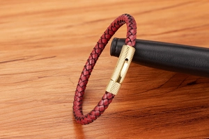 Détail du bracelet en cuir tressé rouge avec fermoir métallique doré moleté sur bois