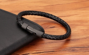 Détail du bracelet en cuir tressé noir avec fermoir métallique texturé sur un portefeuille en cuir