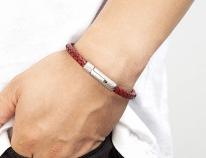 Gros plan d'un bracelet en cuir tressé rouge avec fermoir argenté sur poignet masculin