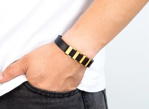 Dettaglio di un bracciale da uomo in pelle nera con cinque barrette di metallo dorato lucido