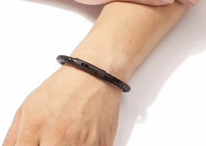 Détail d'un bracelet en cuir tressé noir avec fermoir métallique texturé au poignet