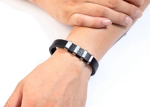 Dettaglio del bracciale in pelle nera con ciondoli in metallo argento sul polso