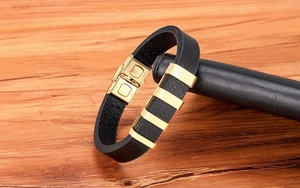 Vista macro di bracciale da uomo in pelle nera con ciondoli in acciaio dorato su supporto