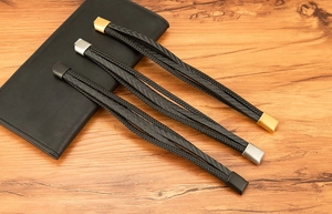 Détail de bracelets multicouches en cuir tressé avec fermoirs magnétiques or, argent et noir