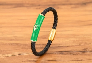 Detalle de pulsera de cuero trenzado negro con dije Evil Eye verde y cierre magnético oro