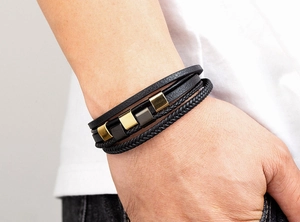 Detail eines mehrlagigen Lederarmbands für Herren mit goldenen und grauen Metallelementen