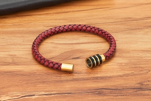 Detail van rode gevlochten leren armband met gouden magneetsluiting op houten ondergrond