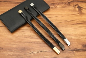 Braided leather bracelets in gold, matte black and silver finishes on a wooden surface