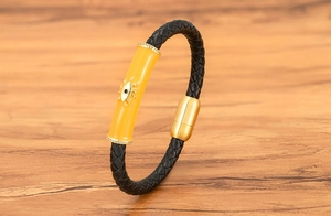 Detalle de pulsera de cuero trenzado negro con amuleto de ojo turco amarillo y cierre dorado