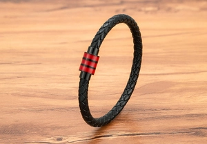Détail d'un bracelet en cuir tressé noir avec un fermoir magnétique en métal rouge et noir