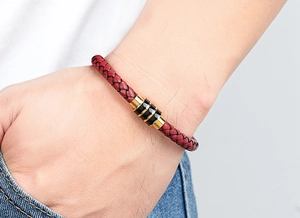 Detail van gevlochten herenarmband in donkerrood leer met zwart-gouden magnetische sluiting
