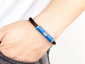 Primer plano de pulsera de cuero trenzado negro con amuleto de ojo de diablo azul en la muñeca