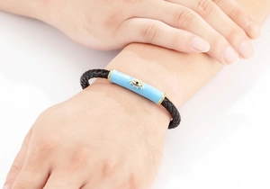 Primer plano de pulsera de cuero trenzado negro con amuleto de ojo malvado en esmalte azul